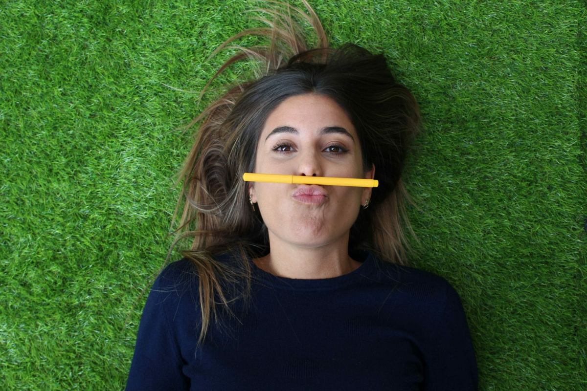 Elisabet tumbada en el césped con un rotulador amarillo sobre el labio, sonriendo a cámara